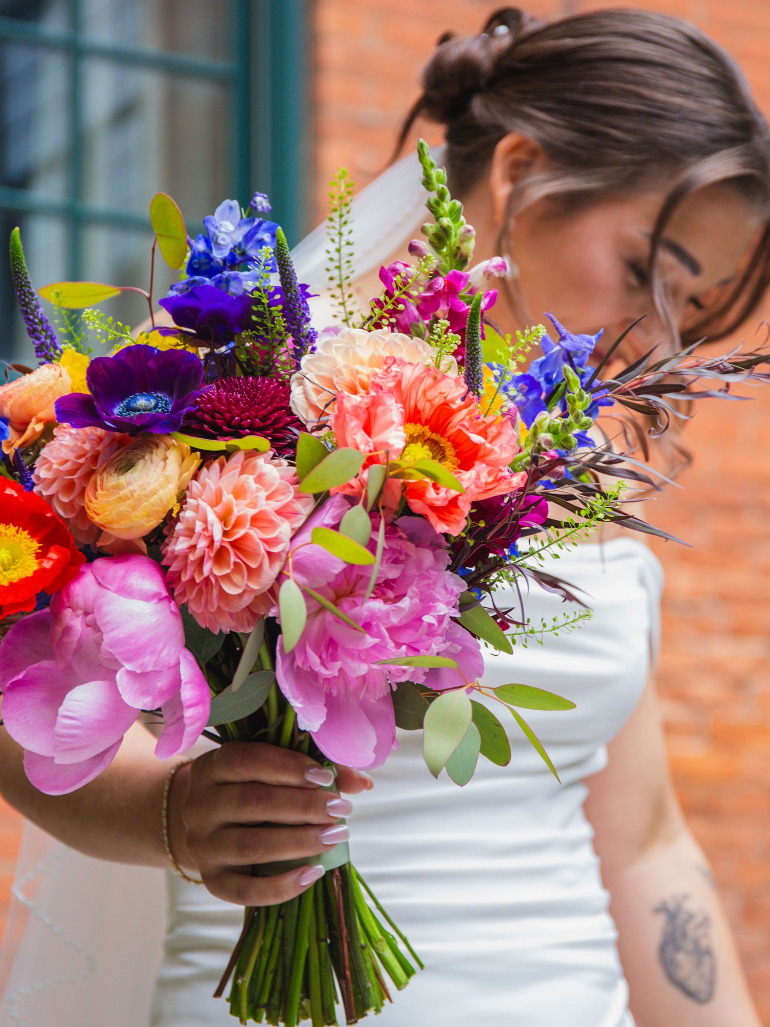 Bride holding a colorful bouquet of peonies, dahlias, and ranunculus